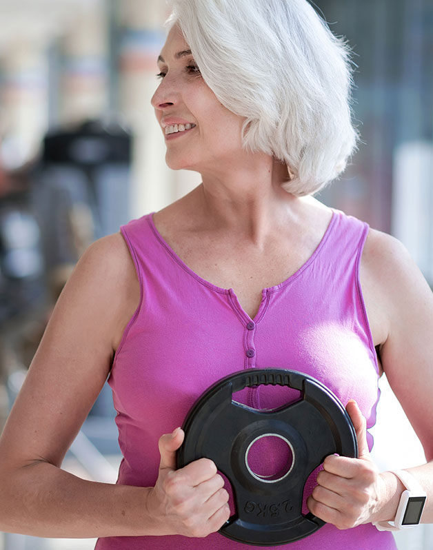 Middle age woman holding weight plate in gym